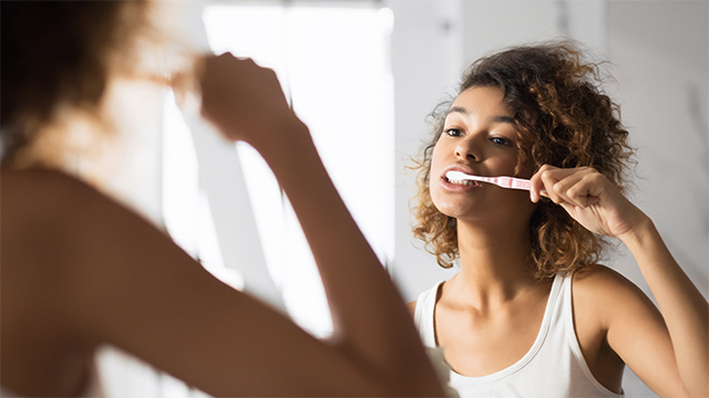 young female brushing her teeth in front of the mirror